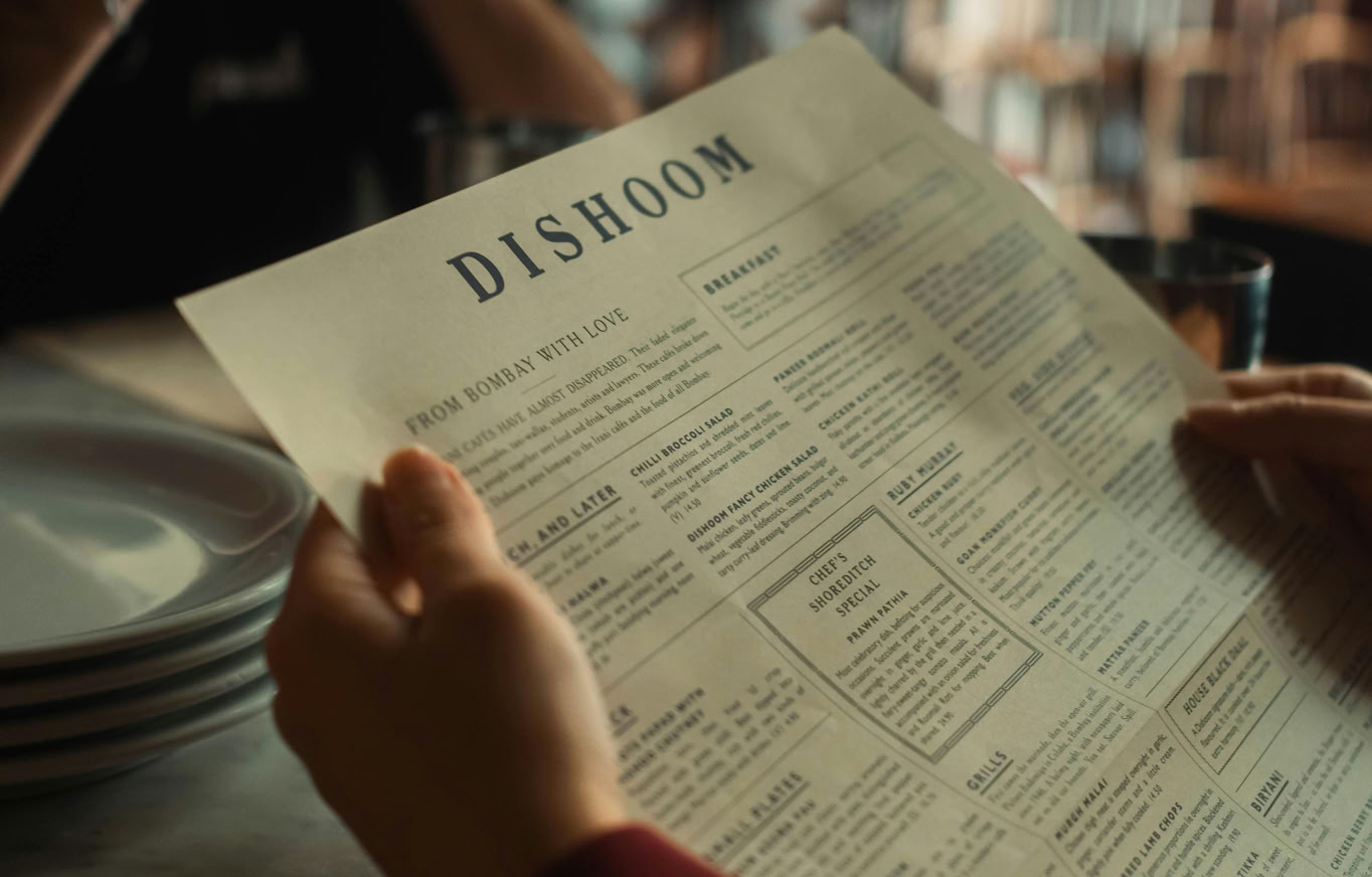 Customer reviewing menu at Dishoom restaurant in warm indoor setting.